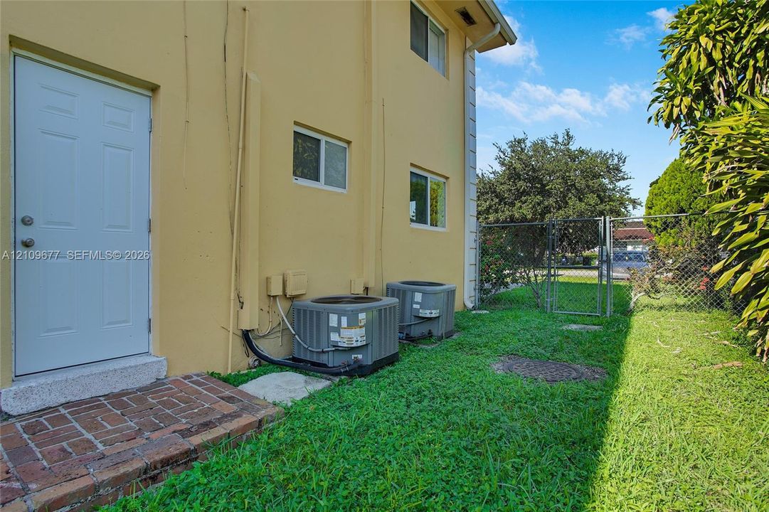 Stucco exterior with brick paver entryway, two exterior HVAC units, and fenced side yard