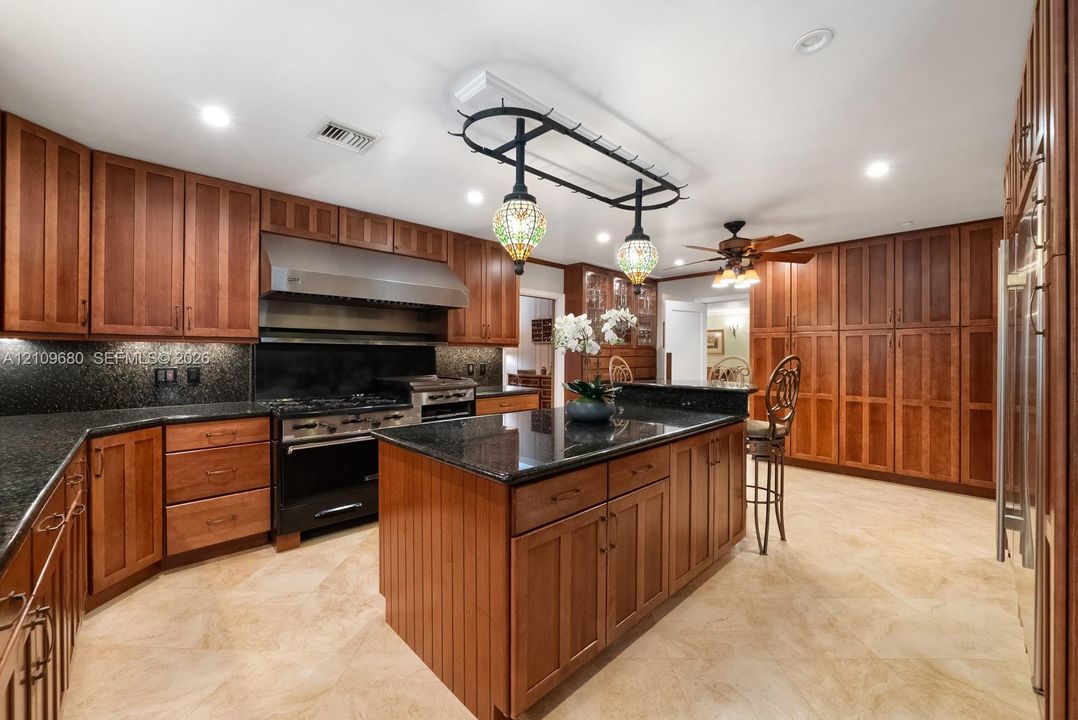 Kitchen featuring custom wood cabinetry, dark stone countertops, an oversized center island, stainless steel professional-grade range with matching range hood, and tile flooring