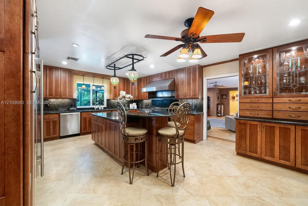Kitchen featuring custom wood cabinetry, central island with stone countertop, stainless steel appliances, glass-front display hutch, and tile flooring