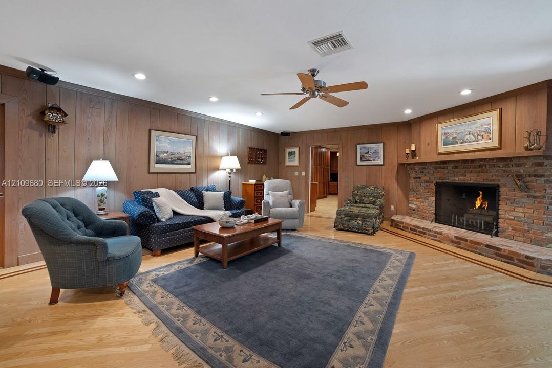 Living area featuring wood-paneled walls, a floor-to-ceiling brick fireplace with a raised hearth, wood-finish flooring, a ceiling fan, and recessed lighting