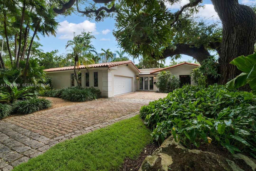 Stucco exterior featuring a terracotta tile roof, paver driveway, multi-pane glass entry doors, and mature landscaping