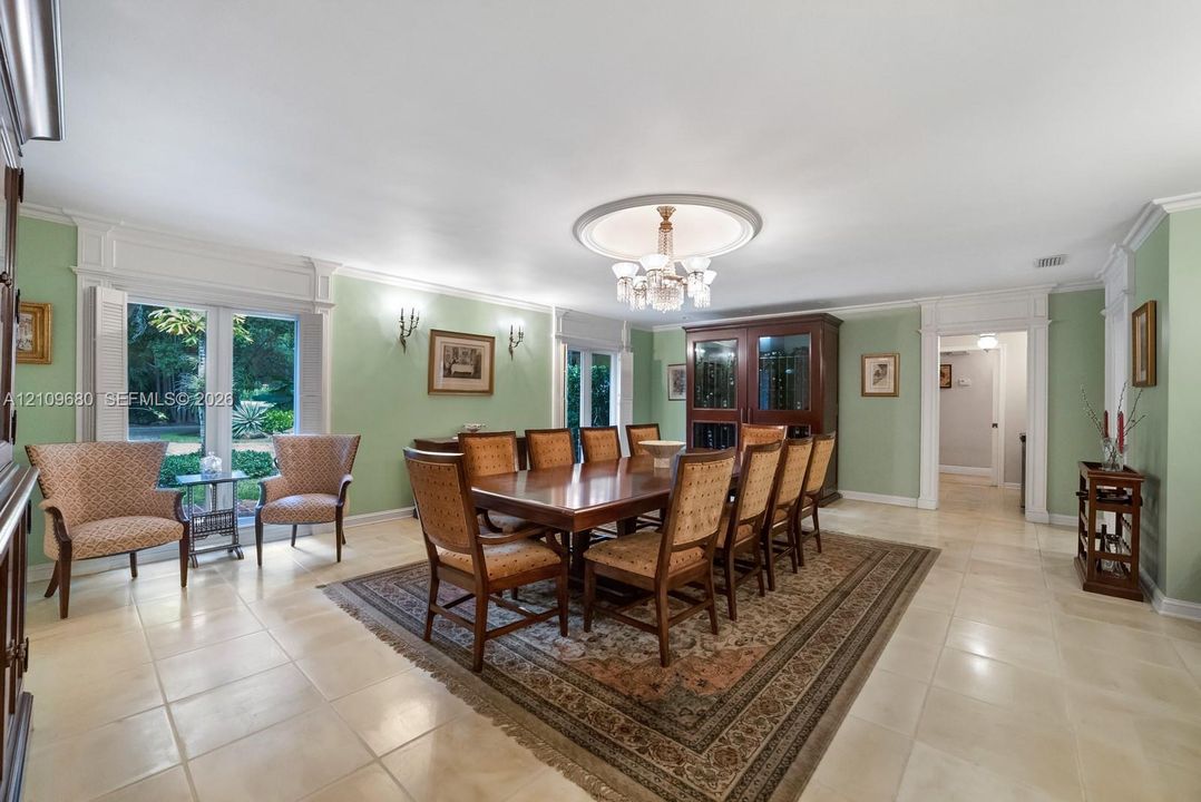 Dining area featuring large-format tile flooring, crown molding, a central ceiling medallion with a tiered chandelier, built-in display cabinetry, and double glass doors with decorative millwork trim