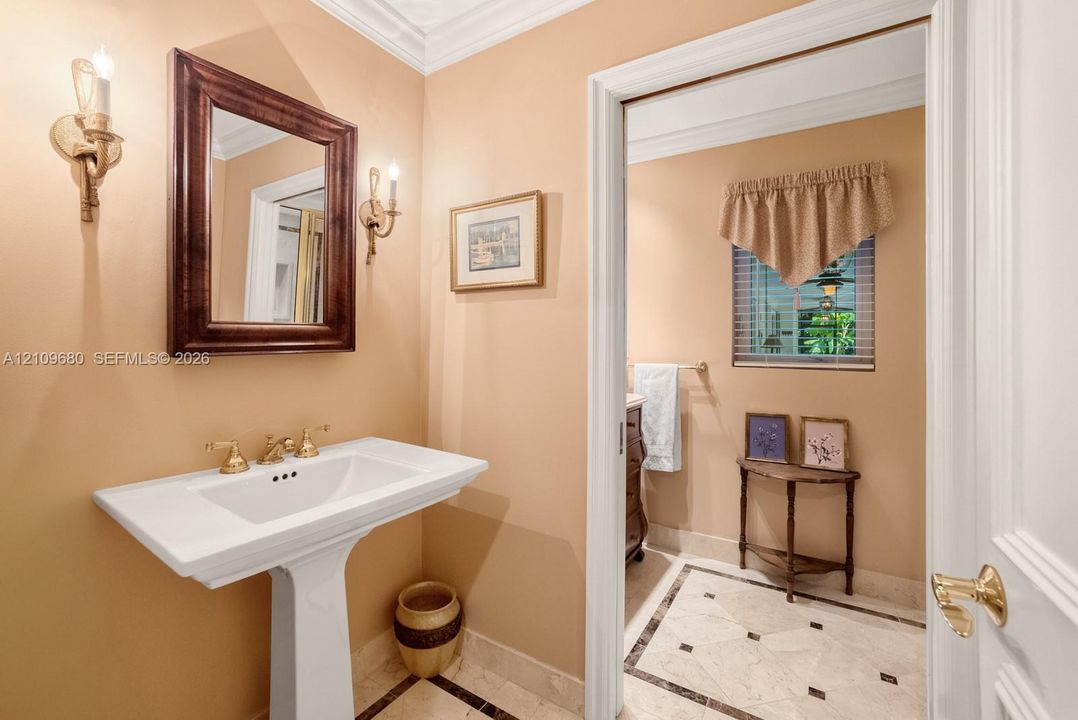 Powder room featuring a white pedestal sink with brass-finish widespread faucet, wall-mounted candle-style sconces, and stone tile flooring with decorative accent inlays