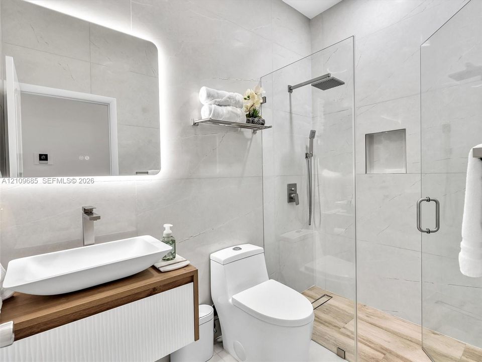 Floating vanity with integrated vessel sink, illuminated LED mirror, floor-to-ceiling tiled walls, and walk-in shower with rainfall showerhead and recessed wall niche