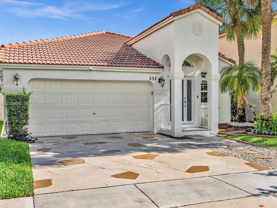 Stucco exterior featuring an arched entryway, decorative stone-patterned concrete driveway, tile roof, and wall-mounted exterior lanterns