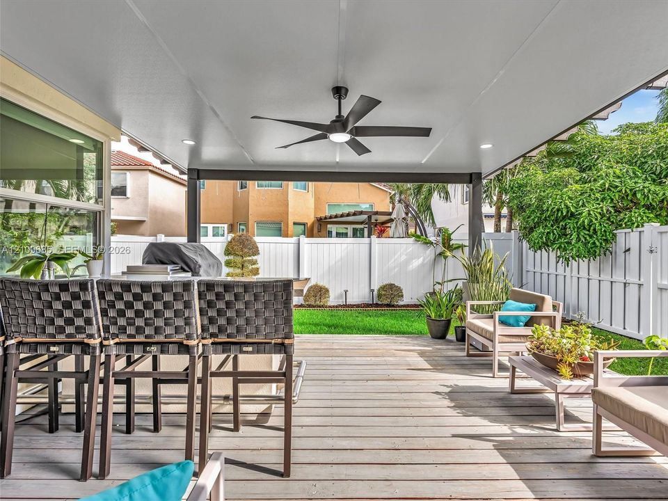 Covered patio featuring a wood-plank deck, built-in outdoor kitchen, ceiling fan with integrated lighting, recessed lighting, and a perimeter privacy fence