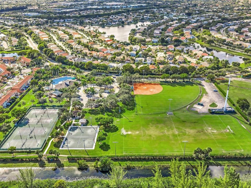 Aerial perspective of a recreational complex featuring multiple tennis courts, a basketball court, a baseball diamond, and a multipurpose athletic field
