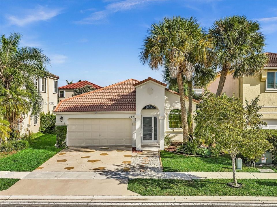 Stucco exterior featuring a tiled roof, arched entryway, attached two-car garage, and decorative stone-accented driveway