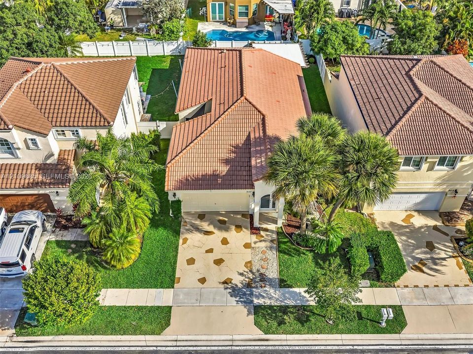 Tile roof, paved driveway with stone detailing, attached garage, and mature palm landscaping
