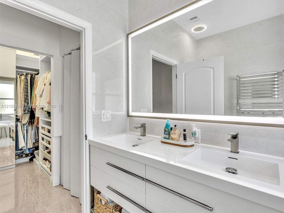 Dual-sink vanity featuring a white countertop, modern rectangular basins, matte-finish hardware, and a large backlit mirror