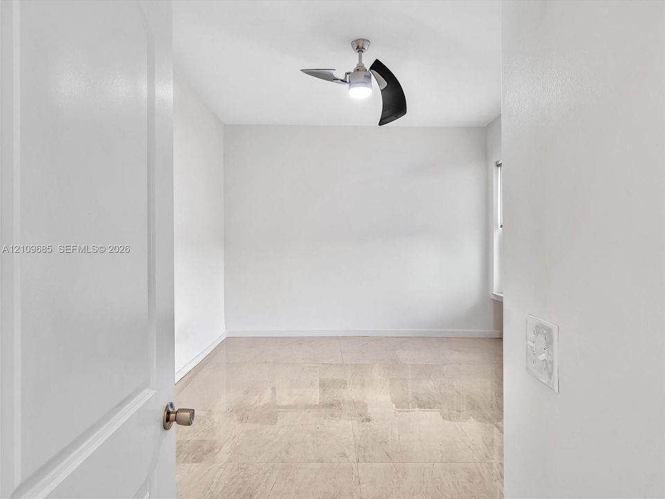 Neutral-toned stone flooring, white walls, and a modern ceiling fan with integrated lighting