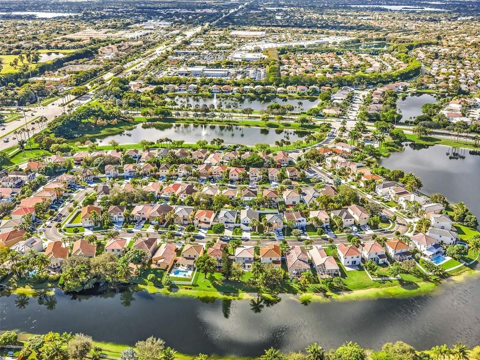 Aerial perspective featuring multi-level residential structures, expansive waterfront frontage, established landscaping, and a curvilinear road network