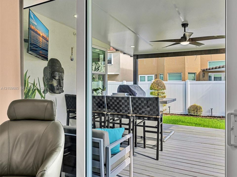Covered patio featuring a wood-finish deck, ceiling fan, recessed lighting, and a white privacy fence