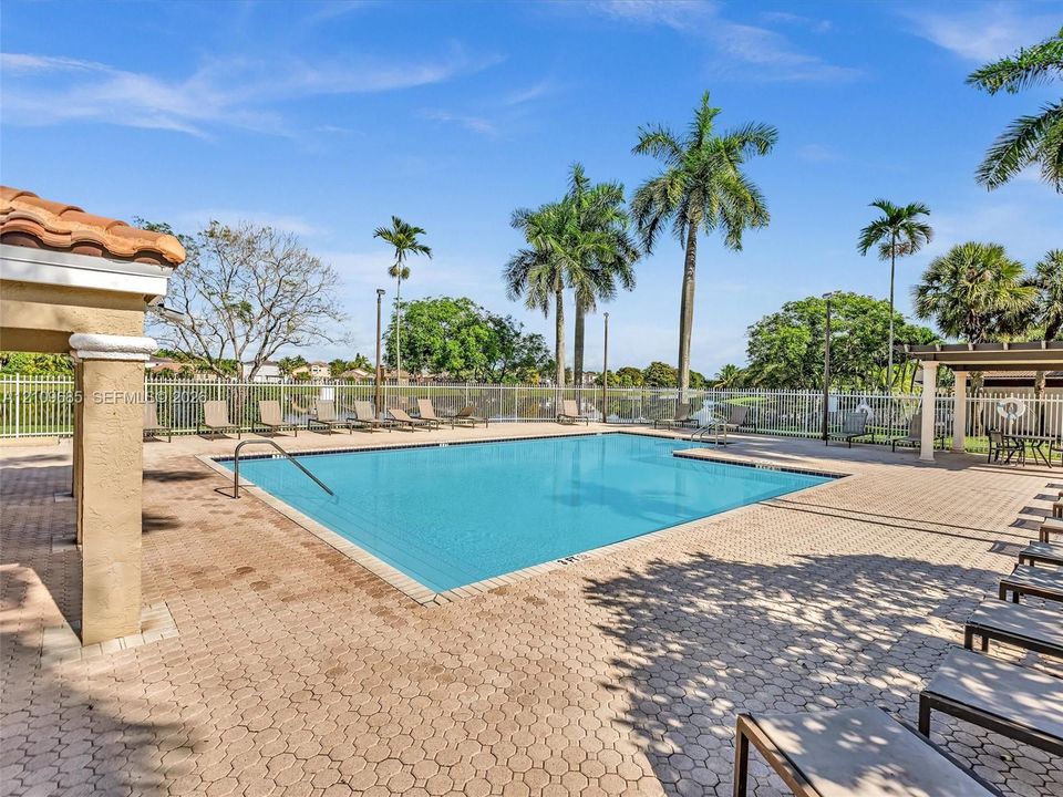 In-ground pool with surrounding paver decking, sheltered poolside pavilion, and metal fencing