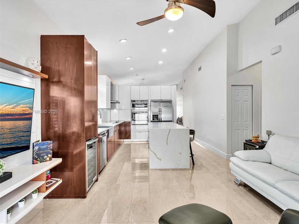 Modern kitchen featuring high-gloss cabinetry, a central island with a stone-finish countertop, stainless steel built-in appliances, a wine refrigerator, and polished tile flooring