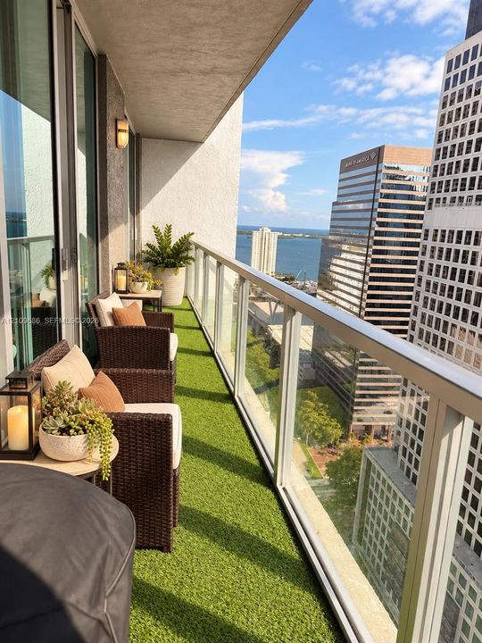Private balcony featuring glass panel railings, synthetic turf flooring, and full-height sliding glass doors