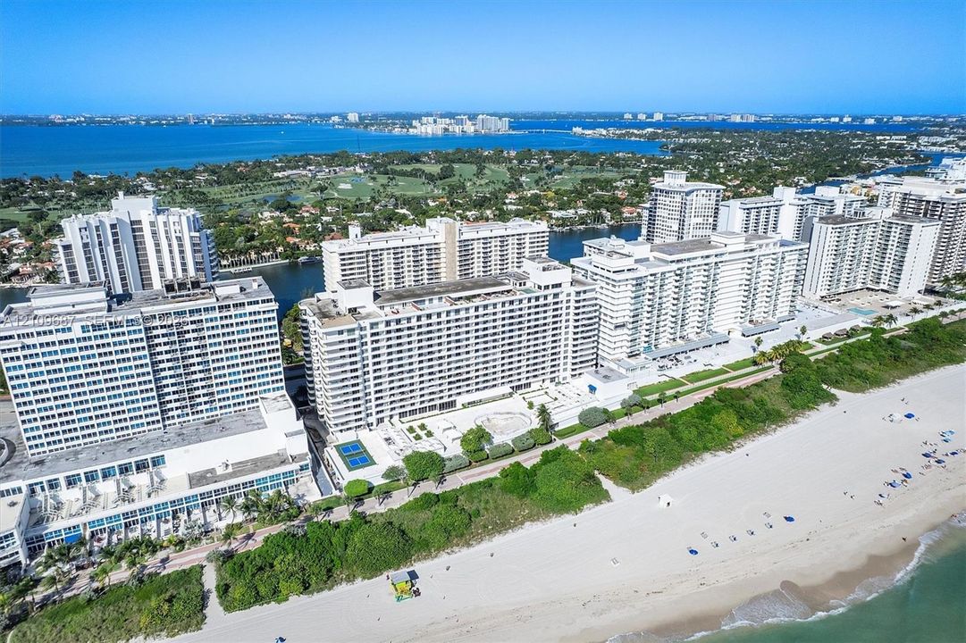 High-rise residential complex situated on a sandy coastline featuring tennis courts, outdoor swimming pools, and paved walkways