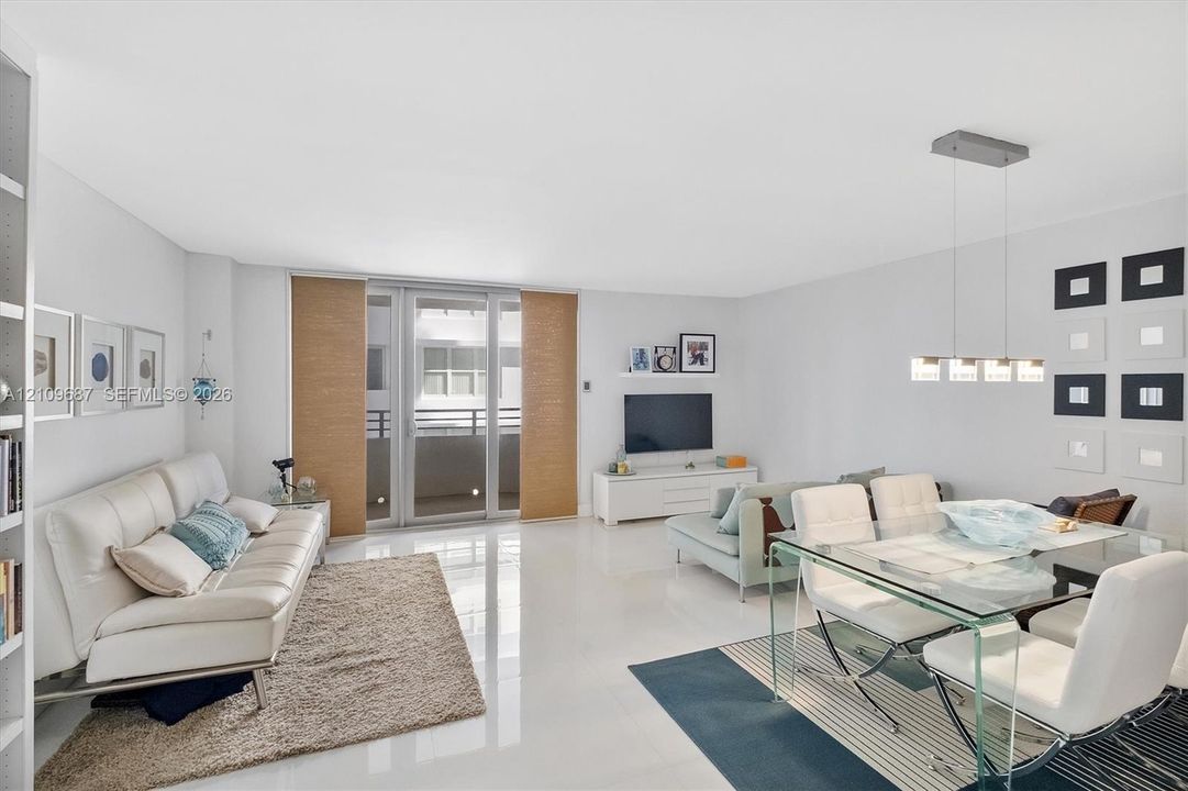 Open-concept living space featuring high-gloss tile flooring, floor-to-ceiling glass sliding doors, integrated wall shelving, and a modern multi-light linear pendant fixture