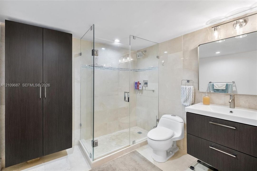 Bathroom featuring a glass-enclosed shower, dark wood-finish cabinetry, a rectangular vanity sink with a metallic faucet, and stone-tile walls