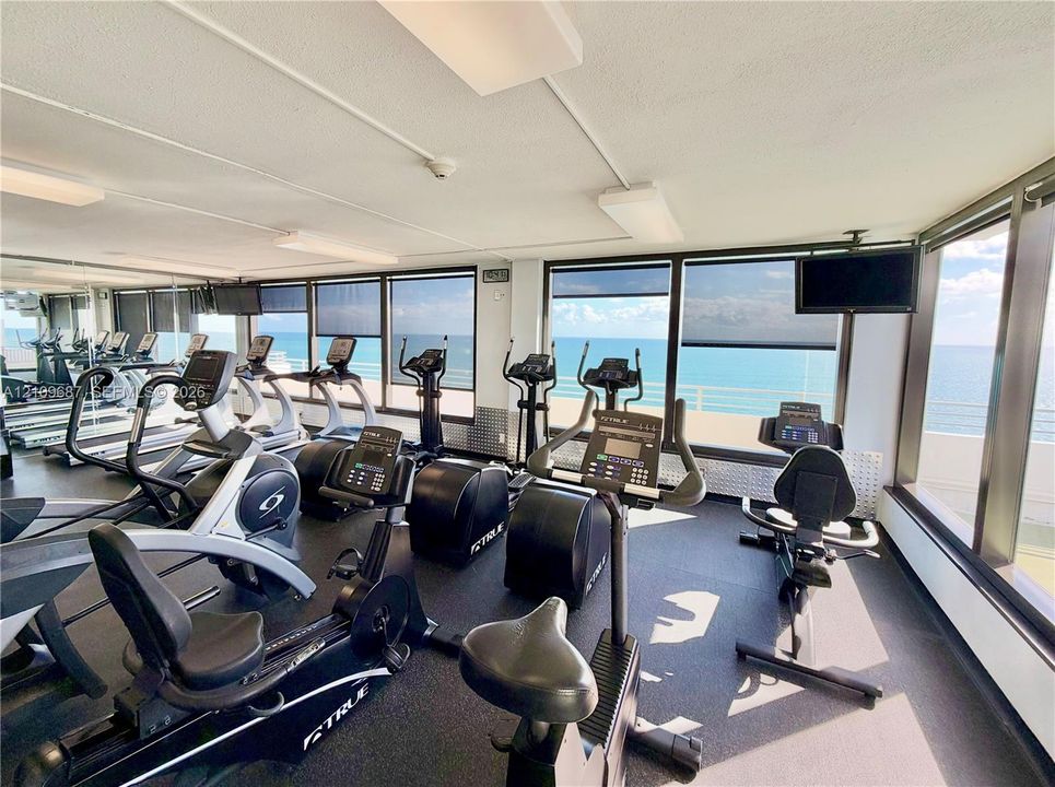 Fitness center featuring rubberized flooring, expansive floor-to-ceiling windows, and wall-mounted televisions