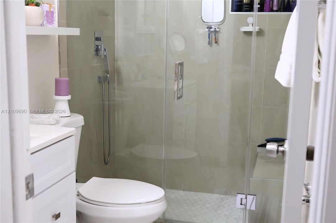 Batroom 2 Walk-in shower featuring a frameless glass door, wall-mounted chrome hand-held shower head, integrated tiled shower bench, and pebble-style floor tiling