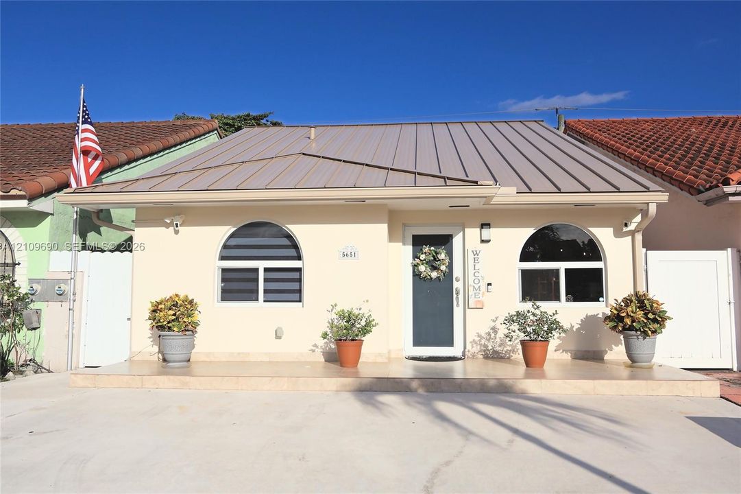 Single-story exterior featuring a metal roof, arched windows, and a tiled front porch