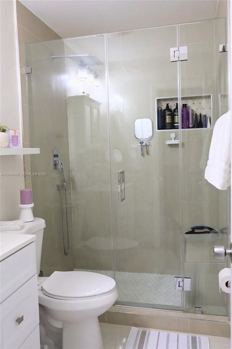 Bathroom 2 Walk-in shower featuring a seamless glass enclosure, rain-style showerhead, handheld sprayer, recessed wall niche, and tiled surround