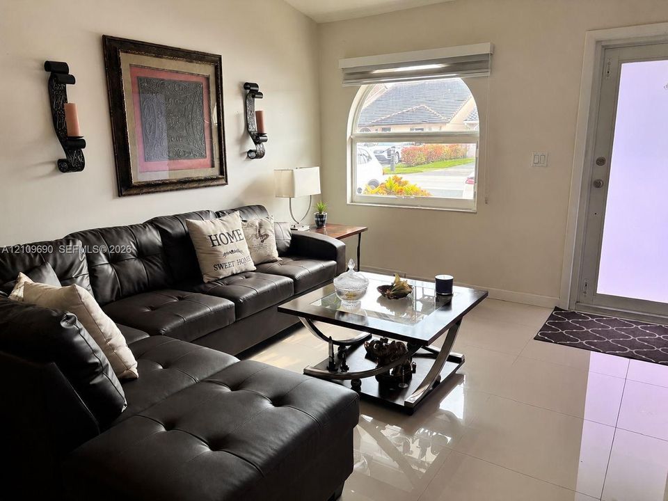 Living area featuring large-format tile flooring, an arched window, and a glass-panel entry door