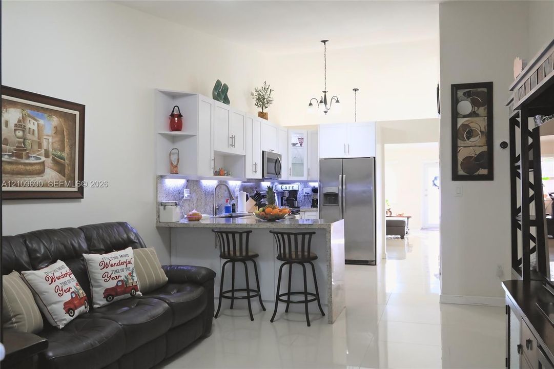 Kitchen featuring white cabinetry, stone-surface countertops, stainless steel appliances, under-cabinet lighting, and a breakfast bar