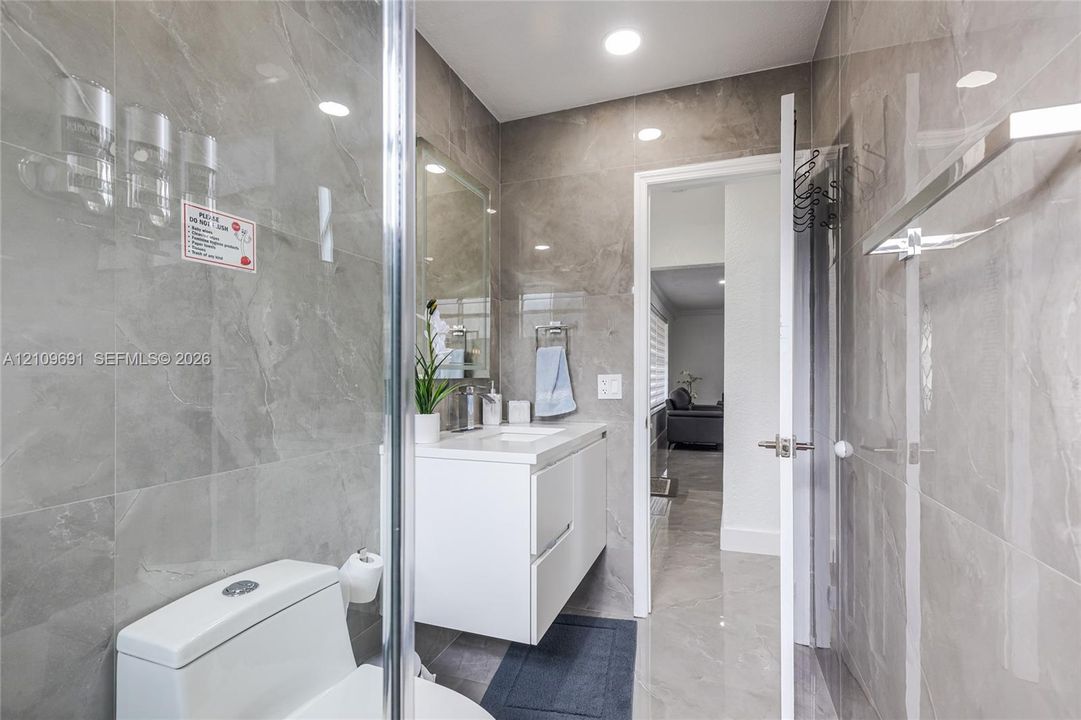 Full-height stone-finish wall tile, floating white vanity, recessed ceiling lighting, glass-enclosed shower, and polished stone-finish flooring