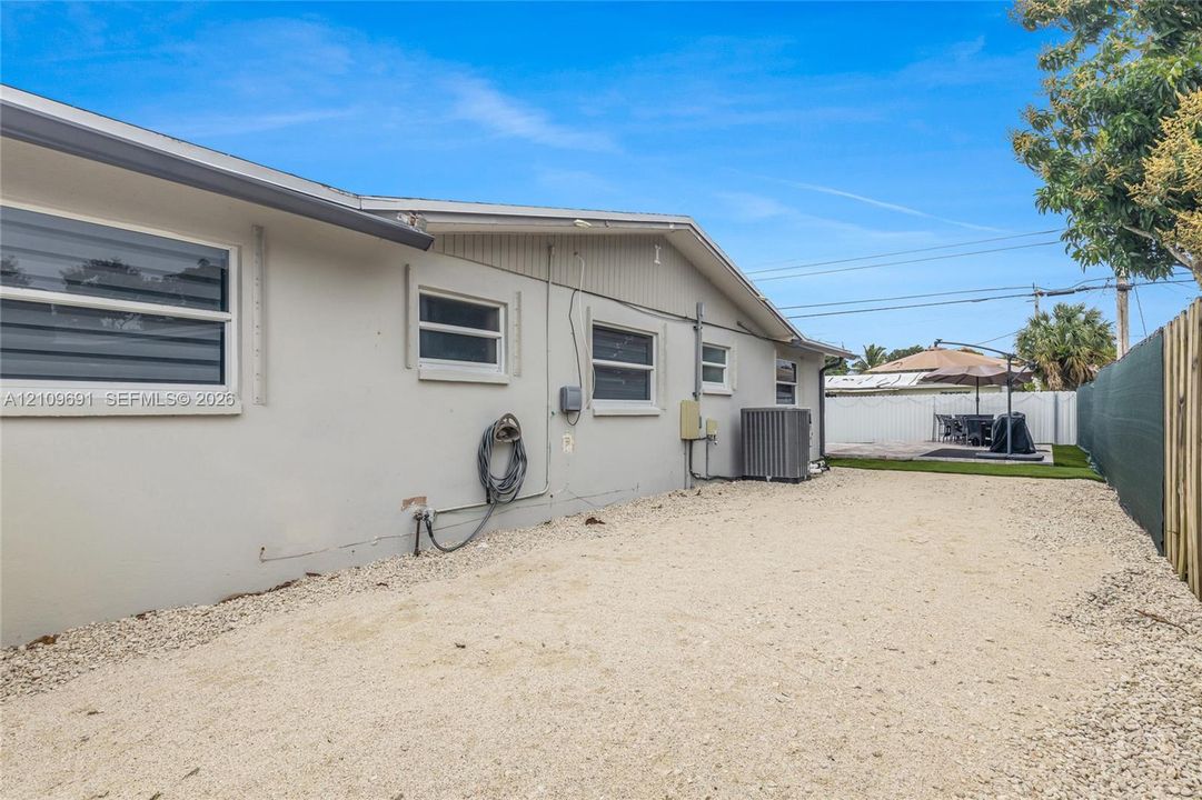 Exterior side profile featuring a light-toned stucco finish, horizontal sliding windows, gravel ground cover, and a privacy fence