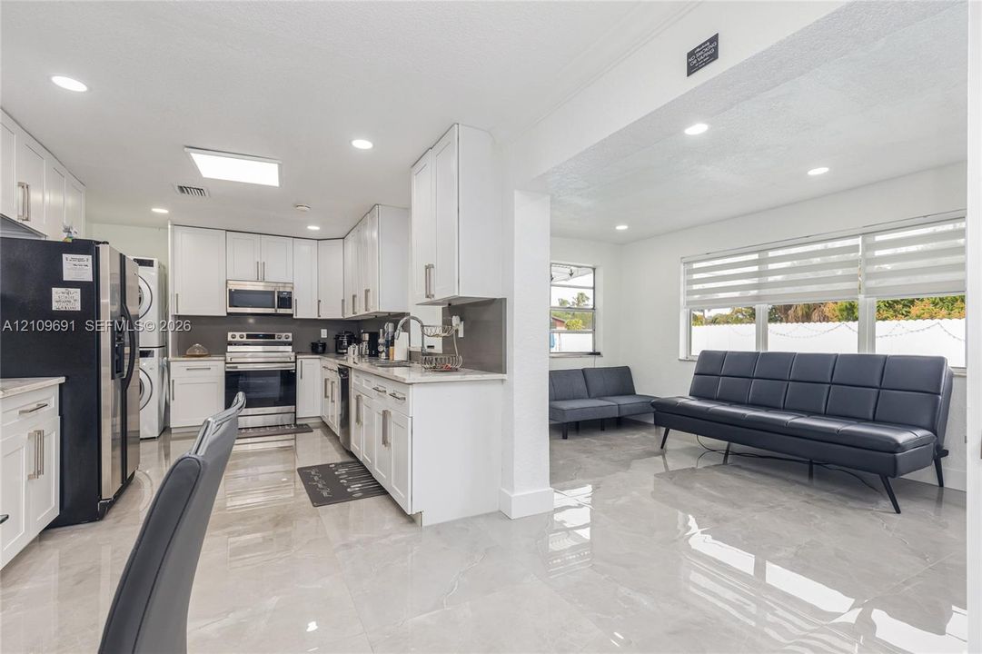 Kitchen featuring white shaker cabinetry, stone-finish countertops, stainless steel appliances, and large-format tile flooring