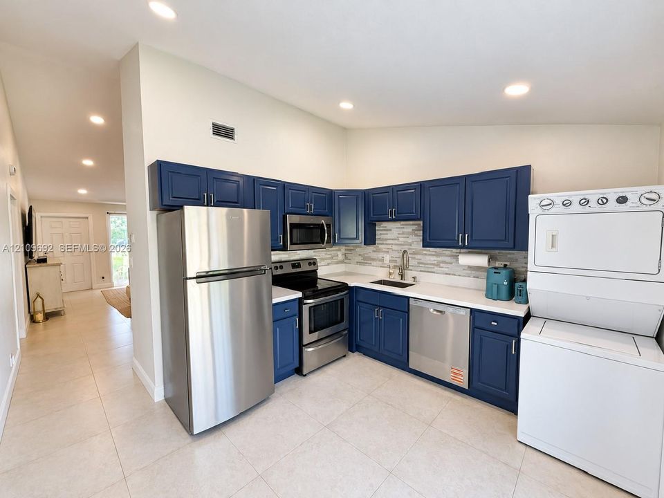 Kitchen featuring dark blue cabinetry, solid surface countertops, a stacked laundry unit, stainless steel appliances, and a tiled backsplash
