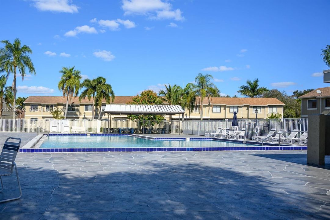 Swimming pool with blue tile border, stone-textured patio deck, covered metal pavilion, and perimeter metal fencing
