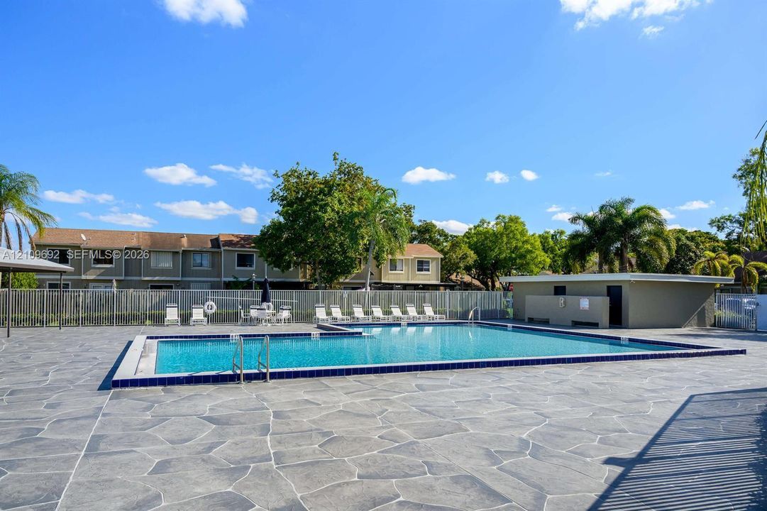 Swimming pool with a tile surround, flagstone-style paved deck, metal perimeter fencing, and an enclosed equipment structure
