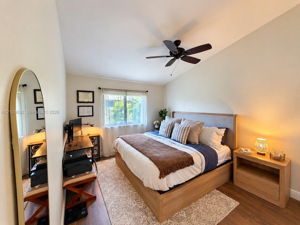 Vaulted ceiling with a matte black ceiling fan, wood-finish flooring, and window with natural light