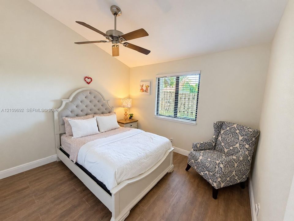 Vaulted ceiling, neutral wall tones, wood-finish flooring, and a ceiling fan with integrated lighting