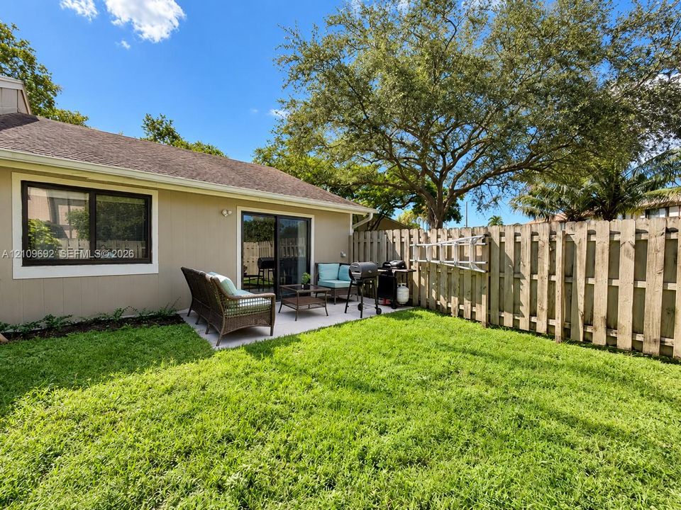 Fenced backyard featuring a manicured lawn, concrete patio, and mature trees
