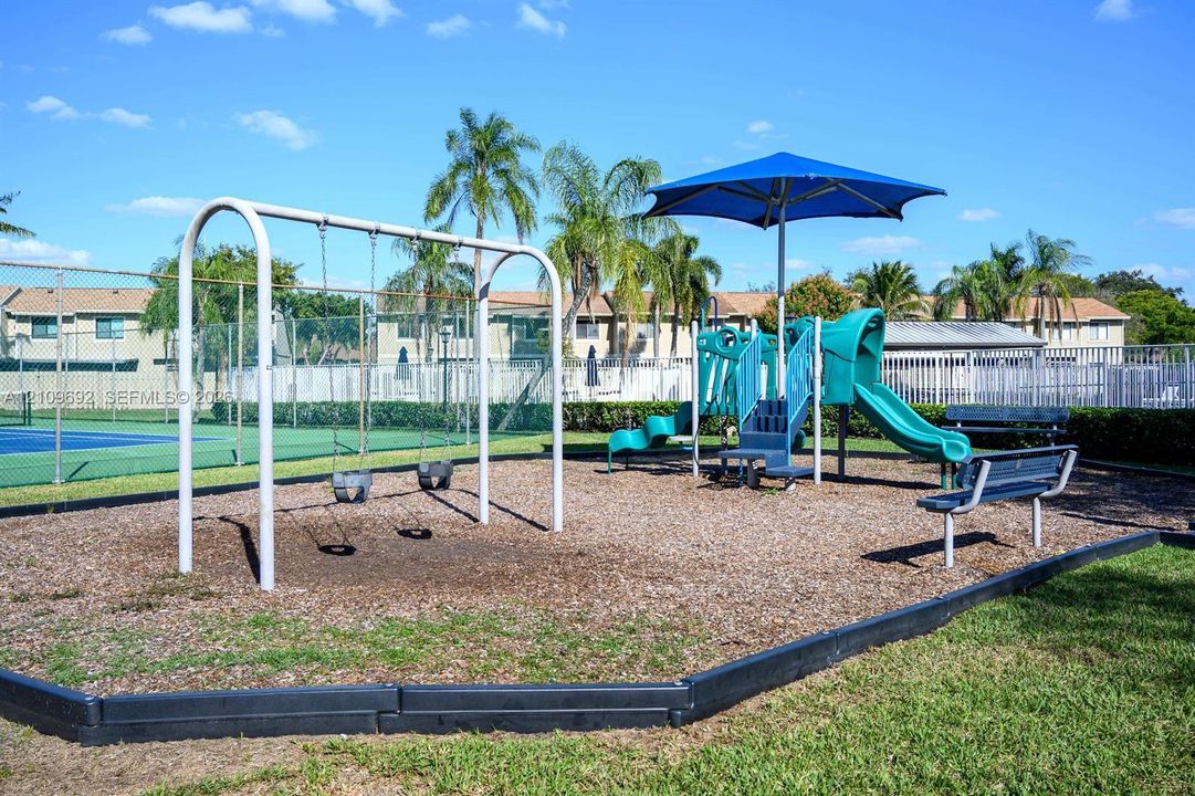 Community recreation area featuring a metal swing set, a structured play system with a sun shade, and stationary benches