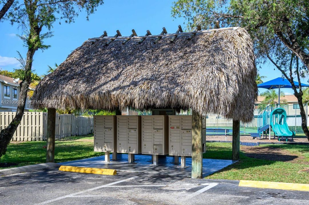 Covered mail kiosk featuring a thatched roof, support posts, and concrete pad