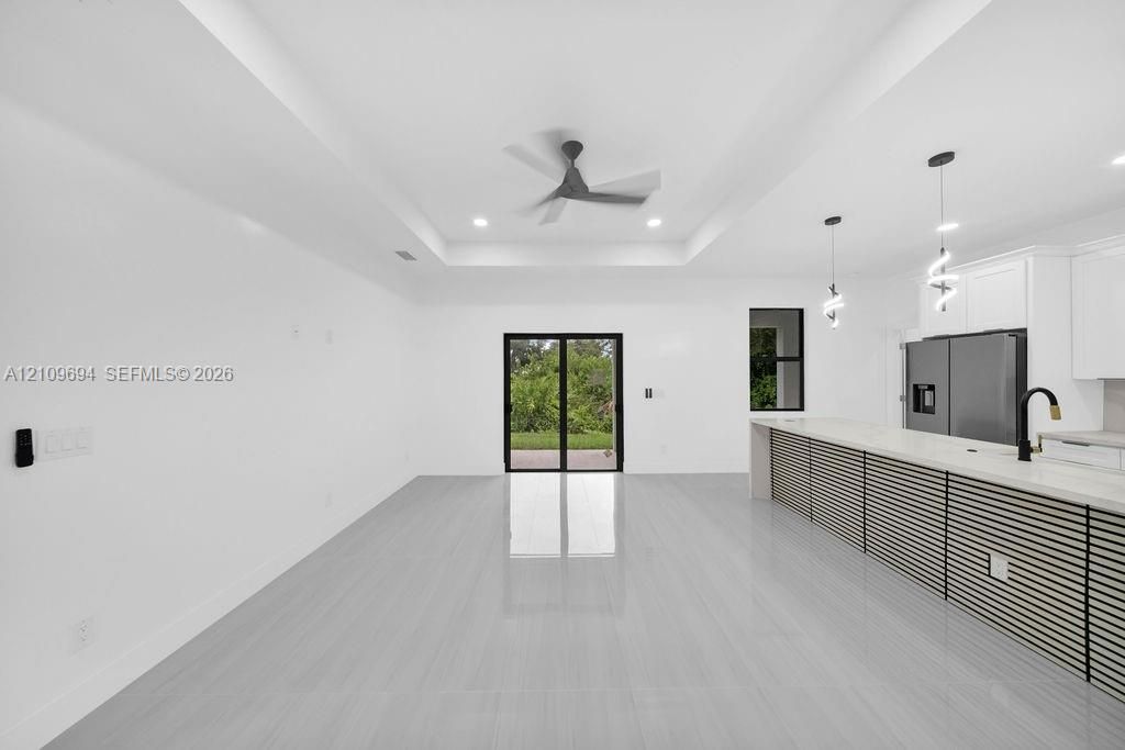 Open-concept interior featuring a recessed tray ceiling, large-format tile flooring, a kitchen island with slat-style detailing and a stone-surface countertop, and sliding glass doors