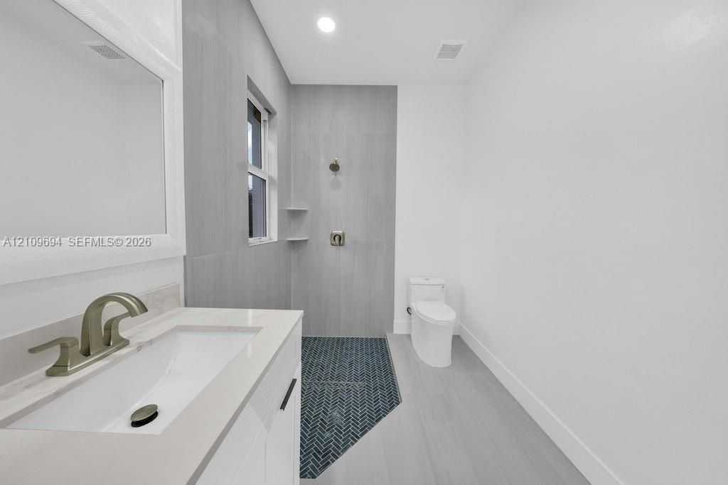 Bathroom featuring a white vanity with quartz countertop, under-mount sink, brushed-finish faucet, shower with grey large-format wall tile, and navy blue herringbone floor tile