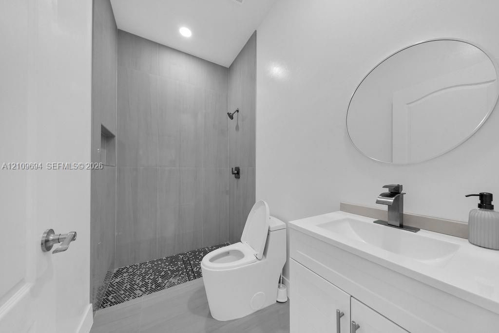 Bathroom featuring a walk-in shower with vertical tile surround and mosaic tile flooring, a modern vanity with integrated sink, a single-handle faucet, and an oval wall-mounted mirror