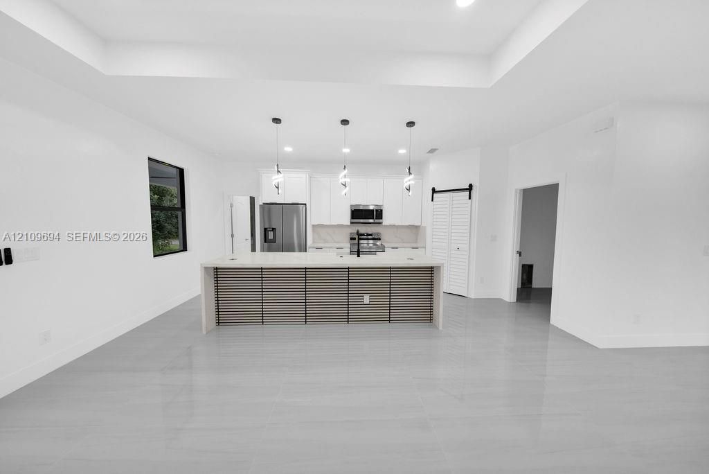 Kitchen featuring white flat-panel cabinetry, a central island with a slatted-wood exterior finish, stone-surface countertops, trio of pendant lights, and large-format tile flooring