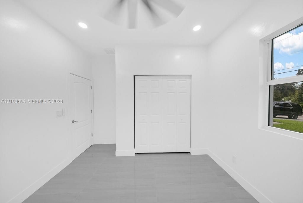 Neutral-toned interior space featuring light grey tile flooring, recessed ceiling lighting, a bi-fold closet, and a single-pane window