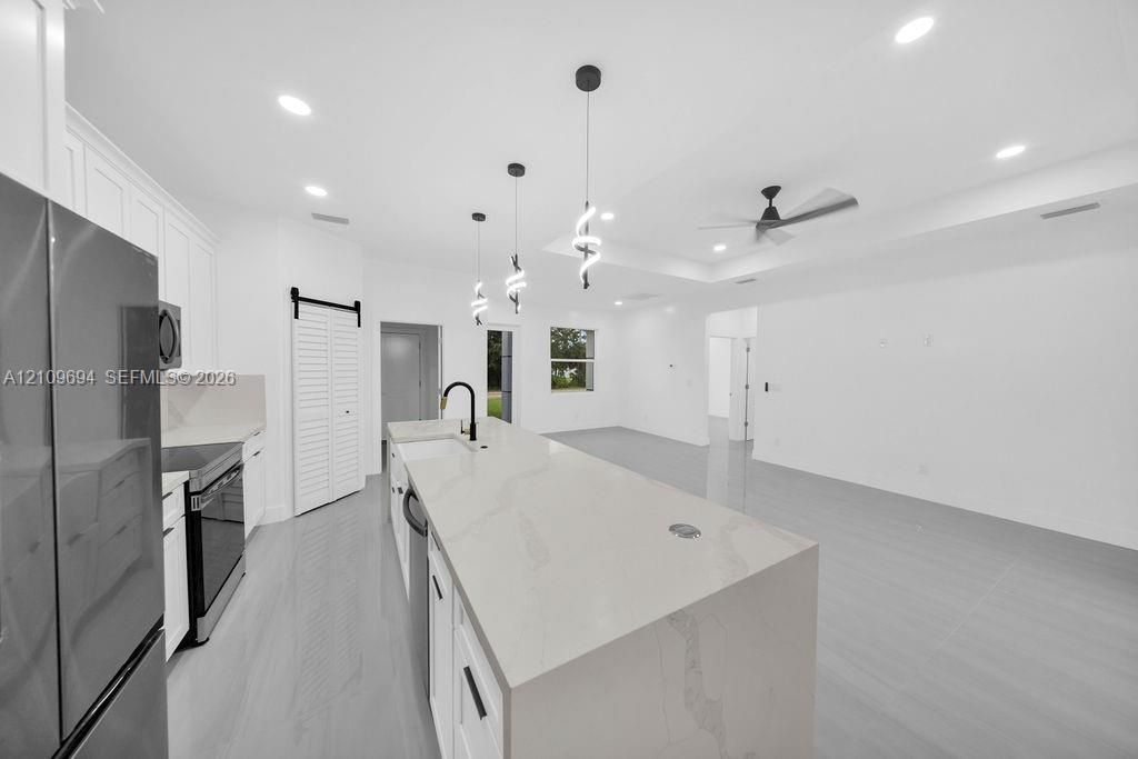 Kitchen featuring an expansive waterfall-edge island, white shaker-style cabinetry, recessed ceiling lighting, decorative pendant fixtures, and a black sliding barn door
