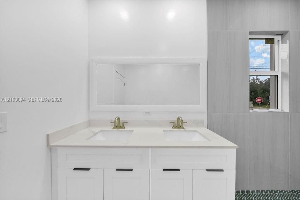 Double vanity featuring white shaker-style cabinetry, quartz countertop, rectangular undermount sinks, brass-toned faucets, and a large framed mirror