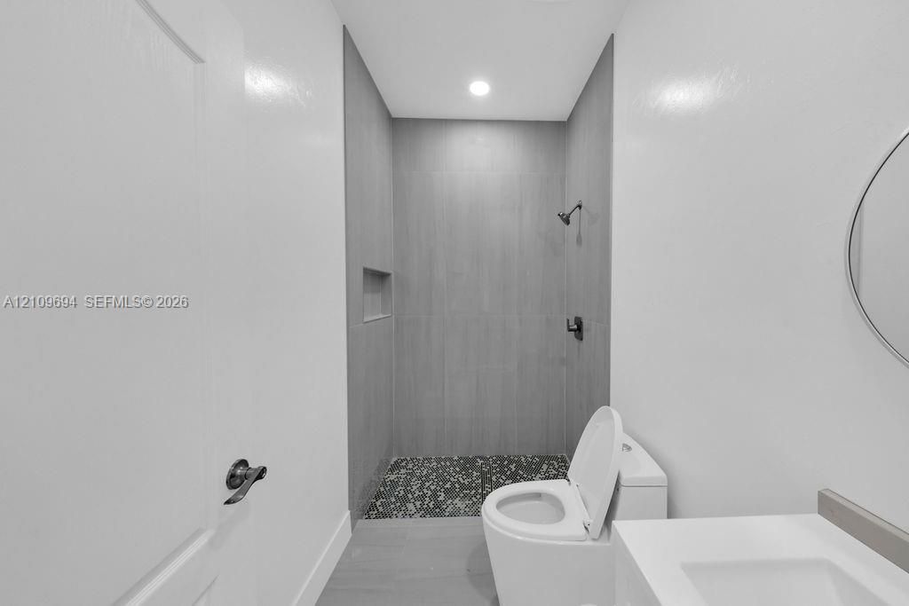 Full-height tiled shower surround with an integrated recessed wall niche, pebble-stone shower floor, matte black shower hardware, and a high-efficiency toilet