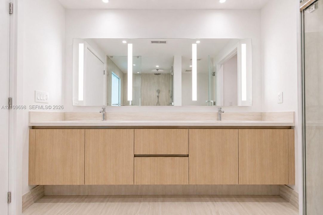 Floating dual-sink vanity featuring light wood-finish cabinetry, solid surface countertop, integrated LED-lit vanity mirror, and polished chrome fixtures