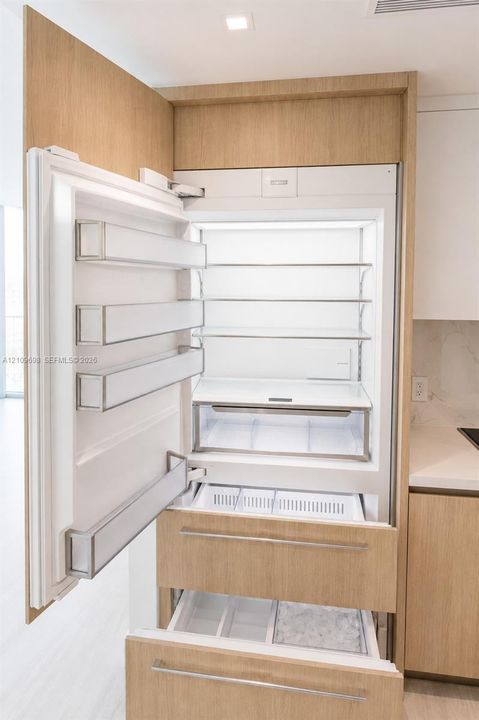 Integrated refrigerator featuring custom wood-finish cabinetry panels, adjustable shelving, tiered pull-out freezer drawers, and recessed lighting